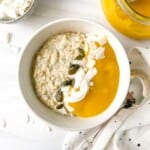 mango oatmeal in a white bowl next to a glass jar of mango puree and a spoon.