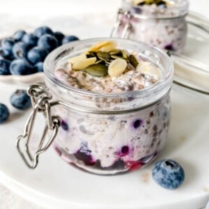 overnight oats with frozen fruit in two glass jars with a bowl of blueberries in the background.