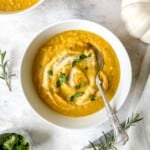 pumpkin cauliflower soup in a white bowl with a spoon in it next to a white pumpkin and rosemary sprigs.