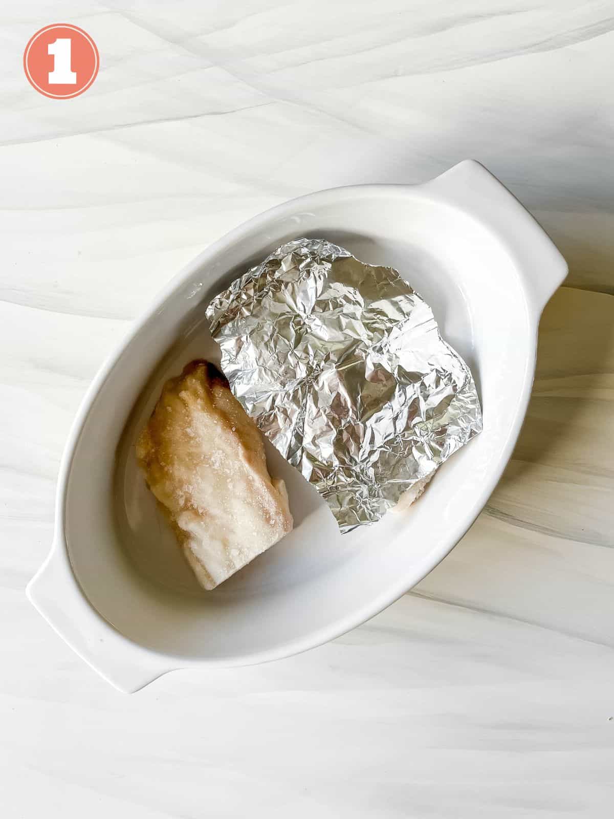 cod fillets in a white dish with one covered by aluminium foil labelled number one.