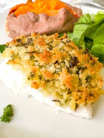 baked cod with panko crust on a cream plate with lettuce and sweet potato.