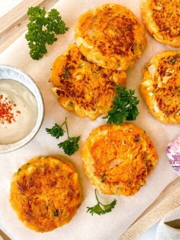 cod and sweet potato fish cakes on a lined wooden board next to a bowl of tahini and herbs.