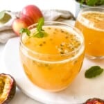 passion fruit mocktail in two glasses next to passion fruits with red apples in the background.