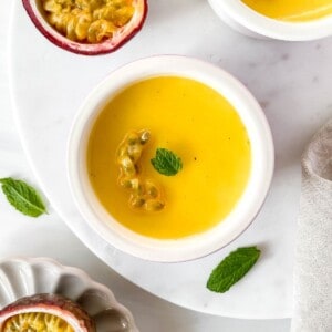 passion fruit posset in two white ramekins next to mint leaves and passion fruit in a bowl.