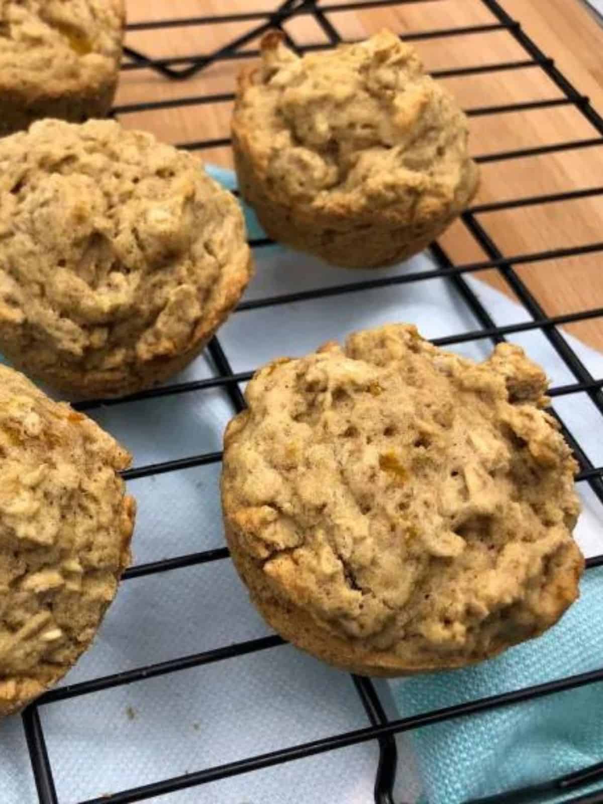 peach oatmeal muffins on a black wire rack with a blue and white cloth underneath it.