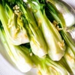 pak choi drizzled with ginger sesame dressing on a white plate with a silver spoon.