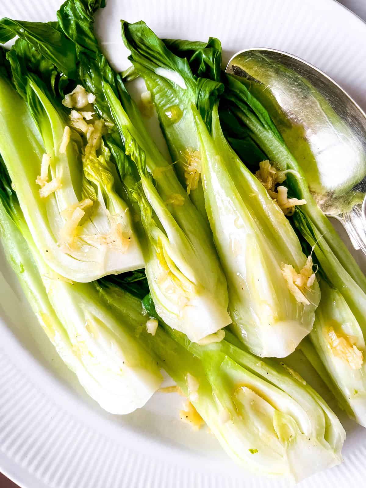 steamed pak choi on a white plate with a silver spoon.