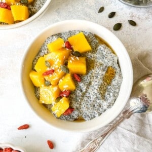 warm chia pudding in two cream bowls next to goji berries and a decorative spoon.