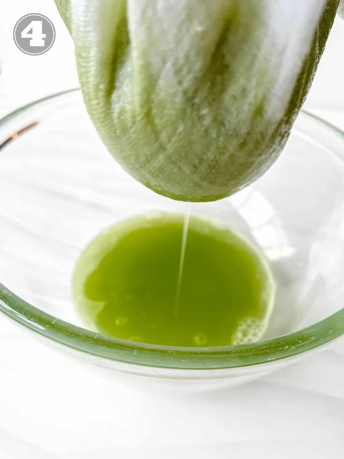 celery cucumber juice being squeezed out of a white cloth into a glass bowl labelled number four.