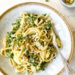 creamy kale pasta in a light grey bowl with a spoon next to a small bowl of pistachios.