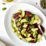 cucumber beetroot salad on a white plate with a silver spoon next to a bowl of pumpkin seeds.