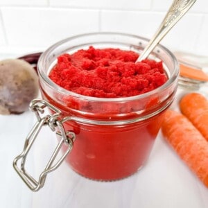 carrot ketchup in a glass jar with a spoon it next to carrots and beets.