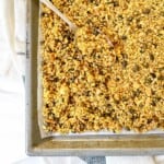 ginger turmeric granola on a baking tray with a spoon on it on a white and blue striped cloth.