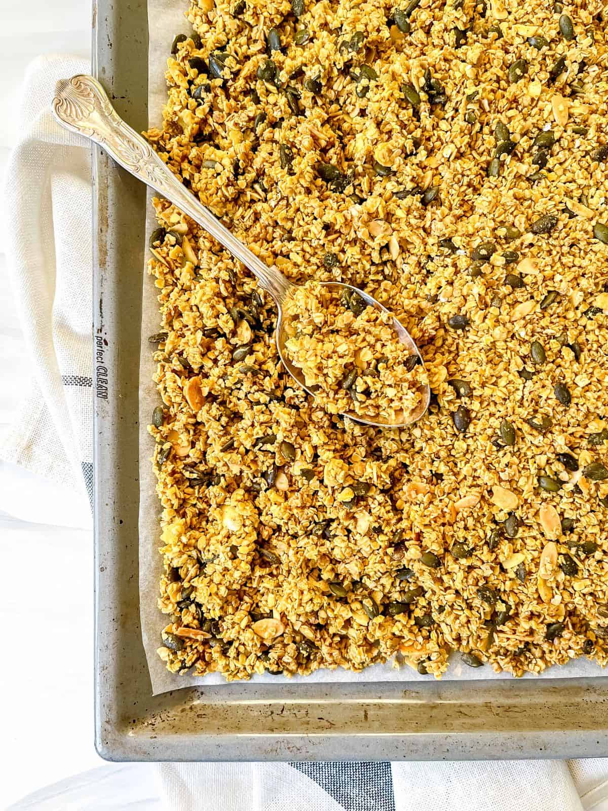 ginger turmeric granola on a baking tray lined with parchment paper with a decorative spoon on it.