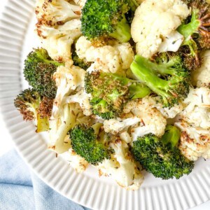 broccoli and cauliflower florets on a cream plate on a blue cloth.