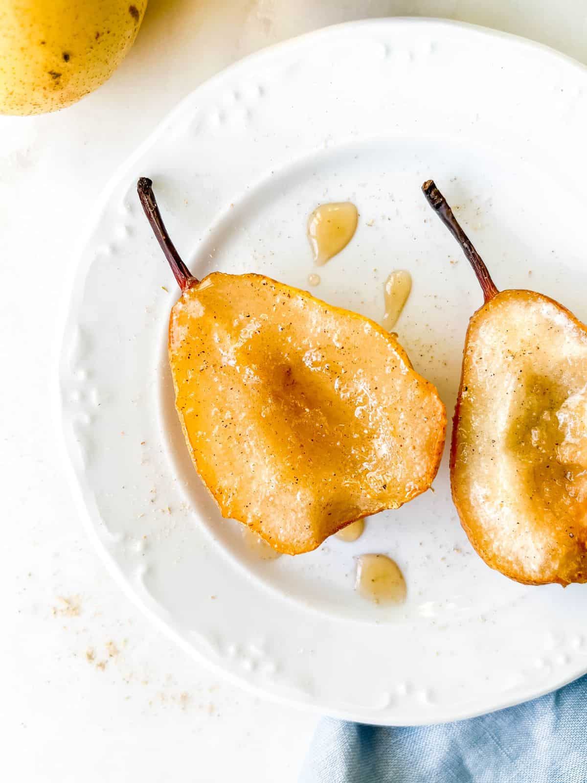 two pears on a white plate drizzled with maple syrup on a blue cloth.
