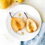 two pear halves on a white plate on a blue cloth next to pears.
