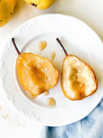 two pear halves on a white plate on a blue cloth next to pears.