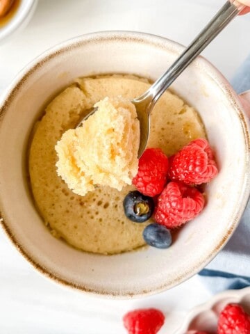 spoonful of honey cake above a mug cake garnished with berries on a blue cloth.