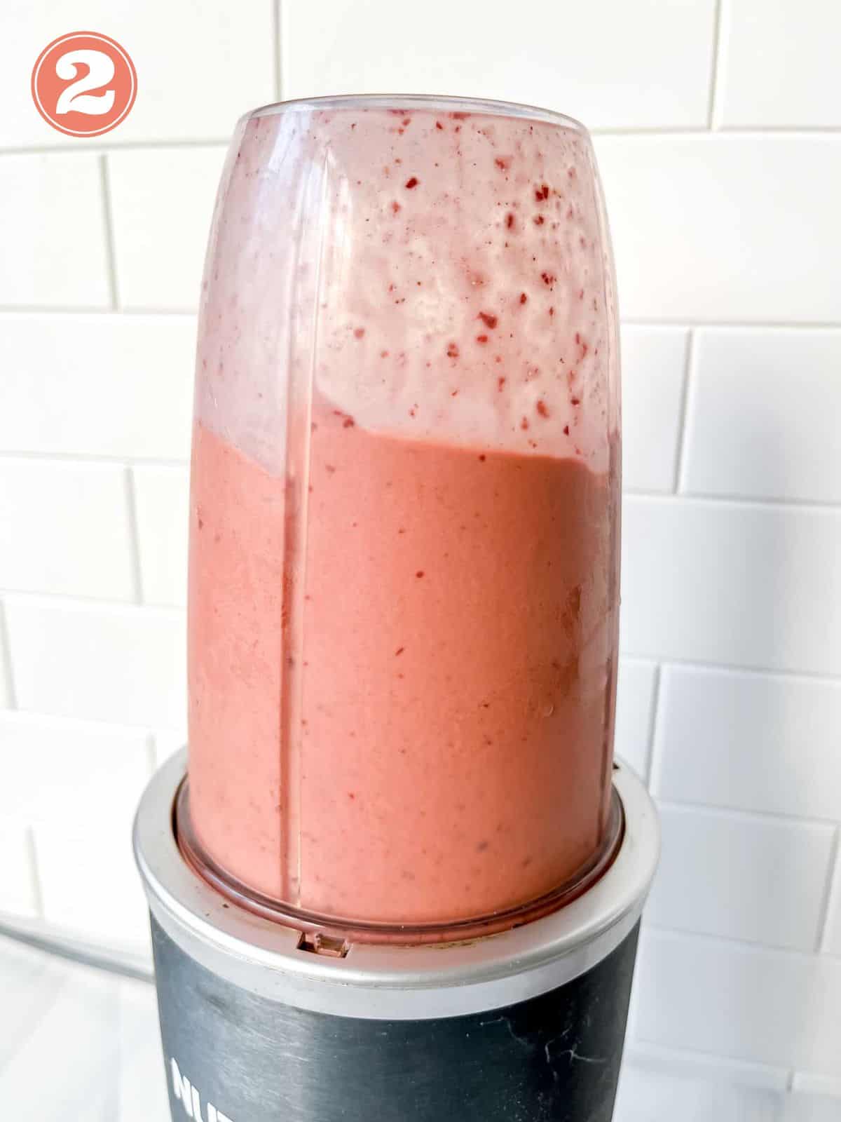 pink smoothie in a blender in front of a white tiled wall labelled number two.