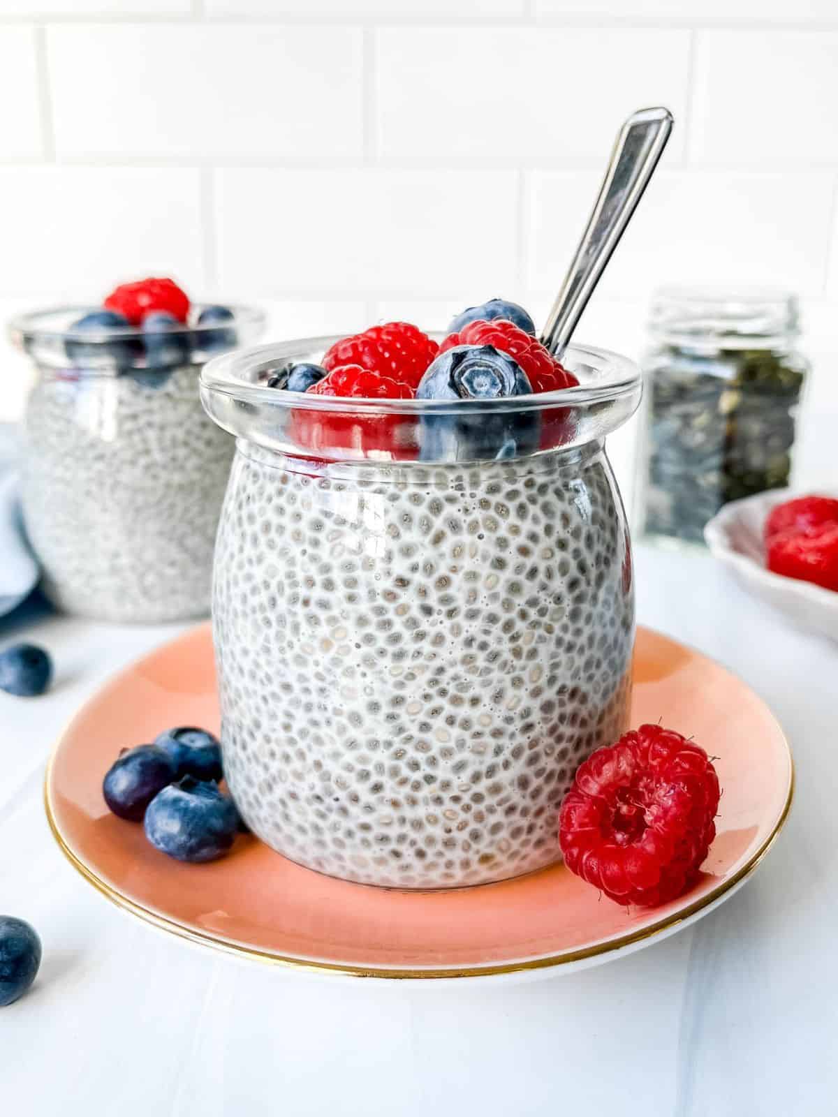 oat milk chia pudding in two glass jars topped with berries and a jar of pepitas in the background.