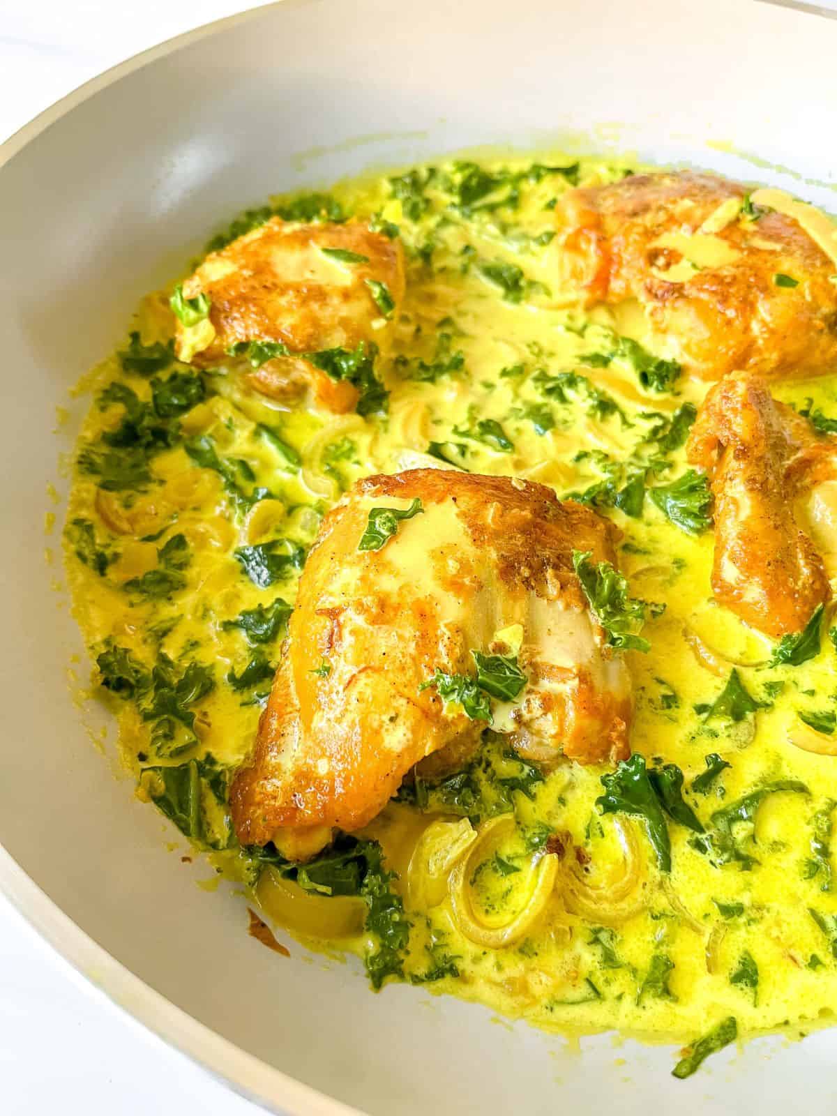 turmeric chicken thighs in a kale cream in a light grey skillet.