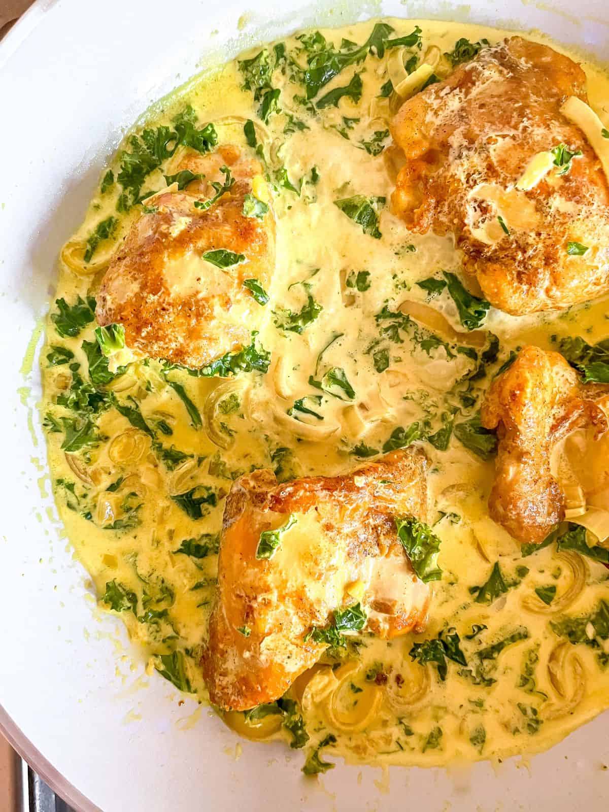 turmeric chicken thighs in a creamy kale sauce in a light grey skillet.