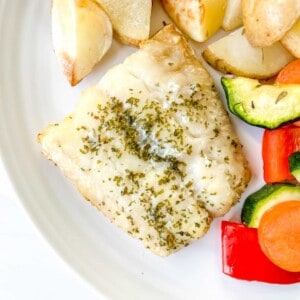 cod fillet, roasted potatoes and vegetables on a white plate.
