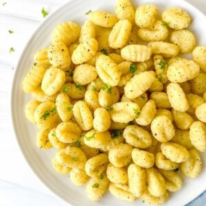 gnocchi garnished with herbs on a white plate on a blue cloth.