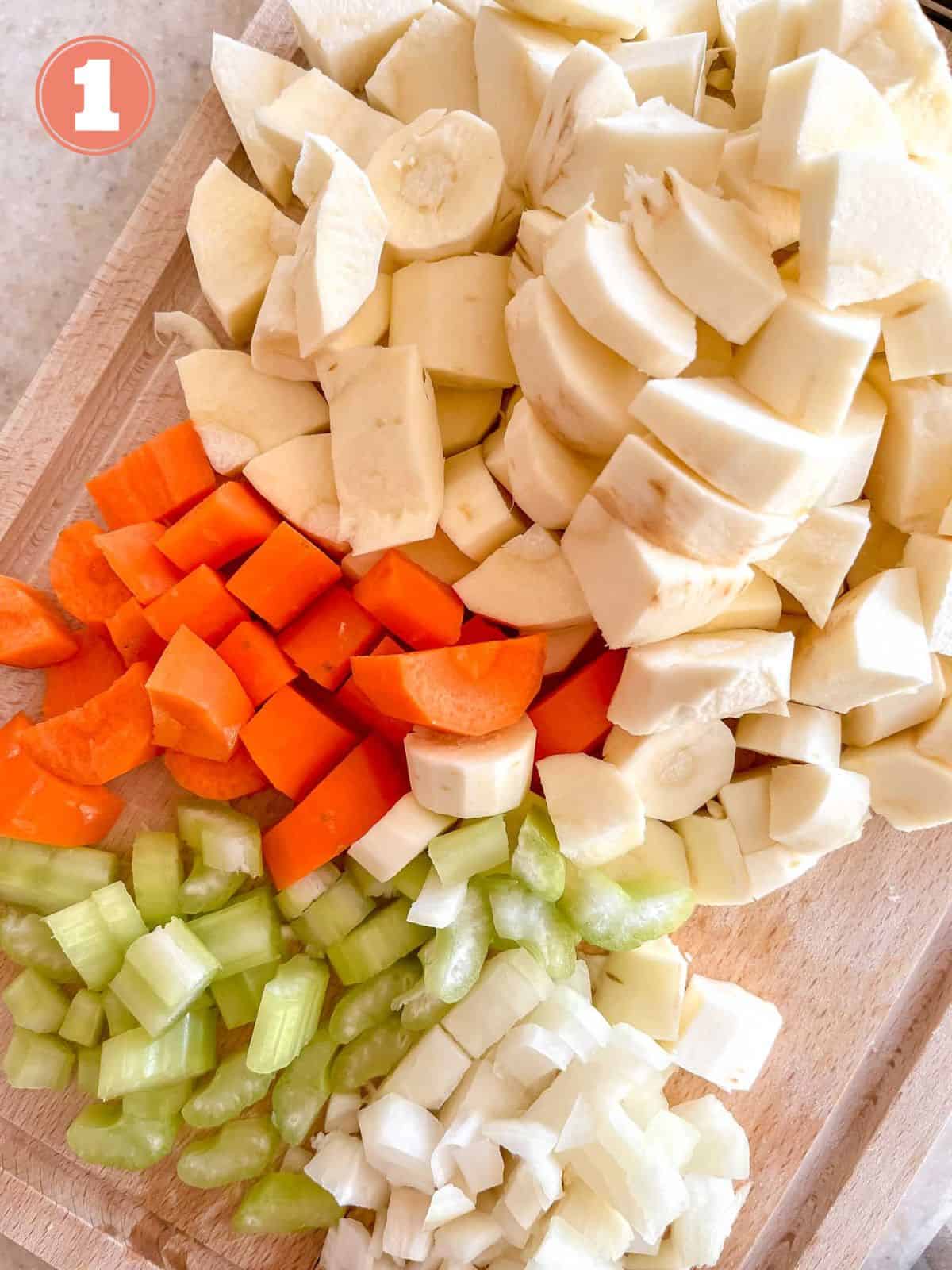 diced parsnips, carrot, celery and onion on a wooden chopping board labelled number one.