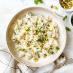 whipped ricotta pasta in a light brown bowl next to cutlery, herbs and bowl of pistachios.