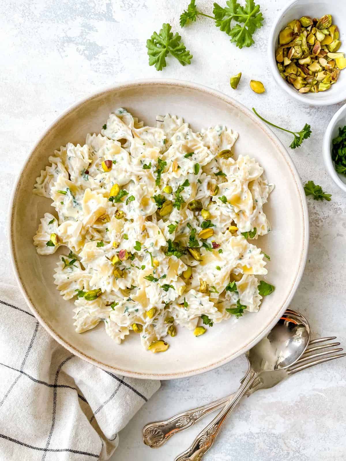 whipped ricotta pasta in a light brown bowl next to cutlery, herbs and bowl of pistachios.