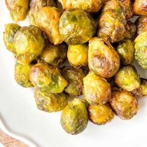 Brussels sprouts on a white plate on a wooden board.