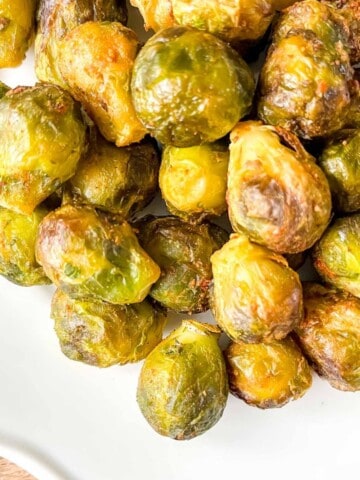 Brussels sprouts on a white plate on a wooden board.