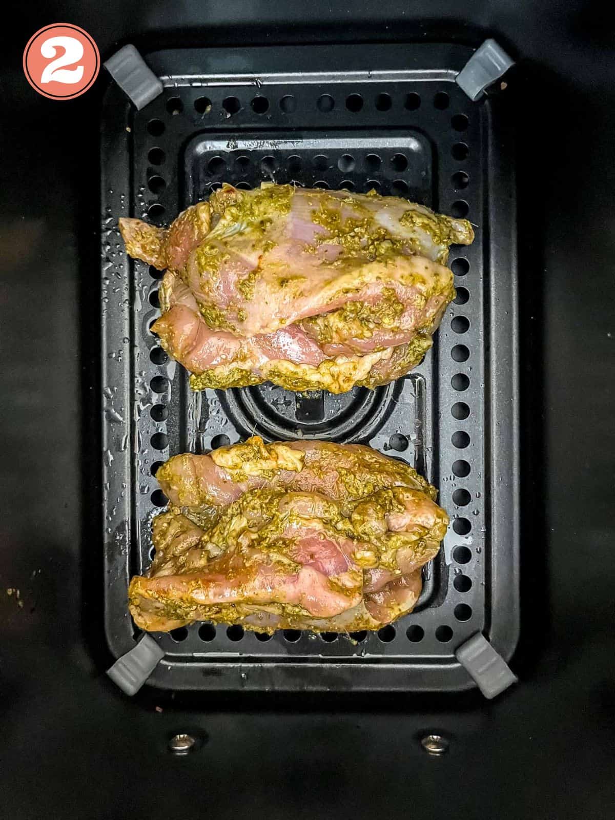 pesto coated chicken thighs in an air fryer basket labelled number two.
