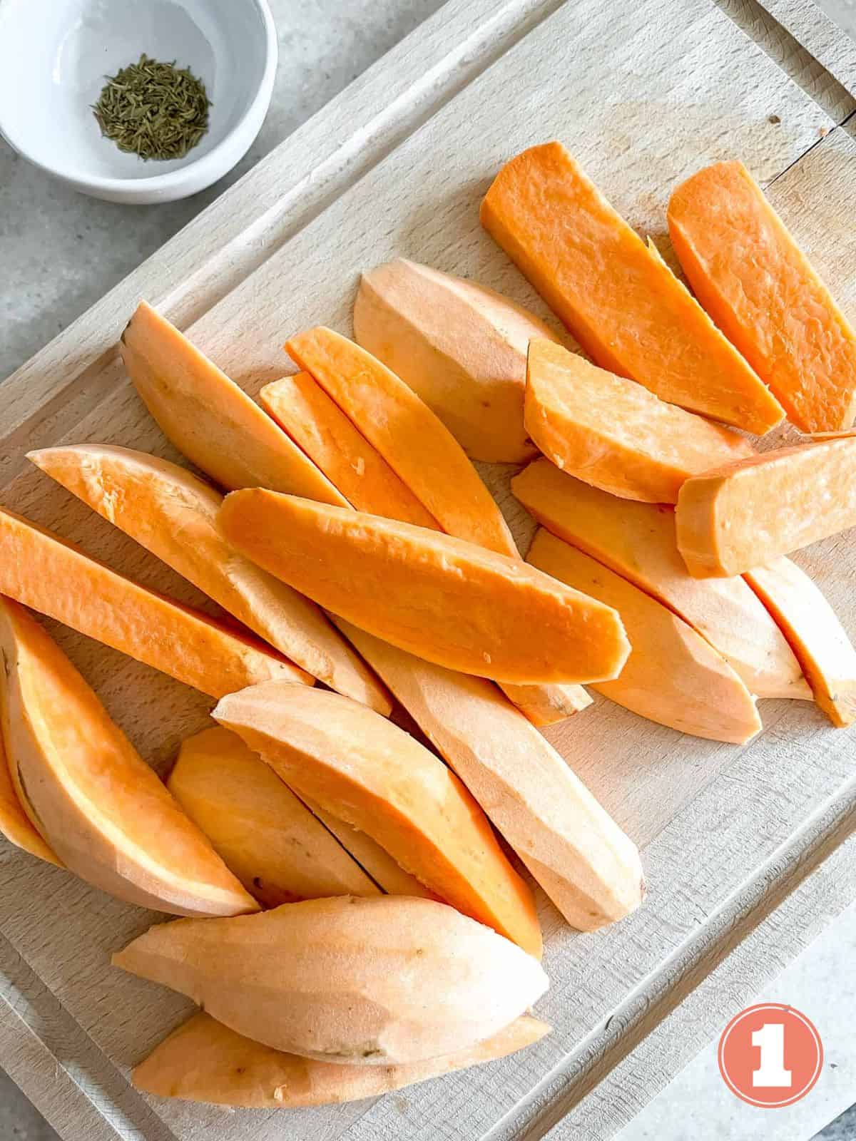 peeled sweet potato wedges on a wooden board next to a bowl of thyme labelled number one.