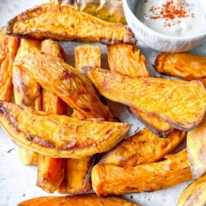 sweet potato wedges on a light grey plate next to a small bowl of tahini.