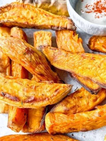 sweet potato wedges on a light grey plate next to a small bowl of tahini.