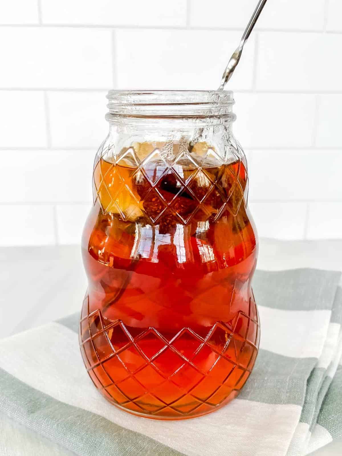 rooibos tea in a pitcher with a muddler in it on a green striped cloth.