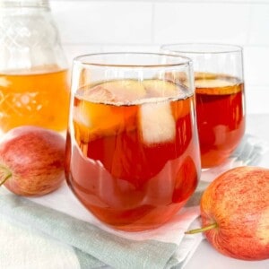 iced rooibos tea in two glasses on a white and green striped cloth next to red apples.