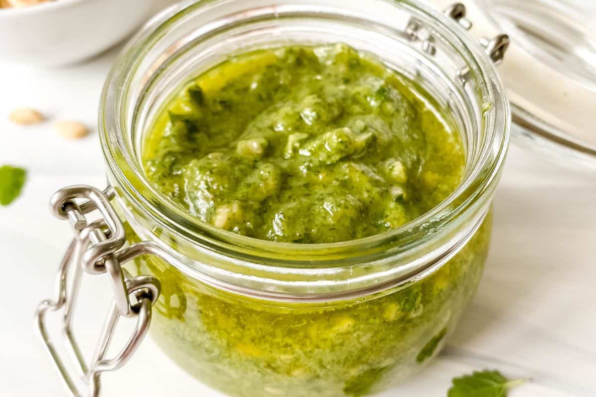 green pesto in a glass jar next to fresh herbs.
