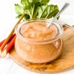 rhubarb puree in a glass bowl on a wooden board next to rhubarb stems.