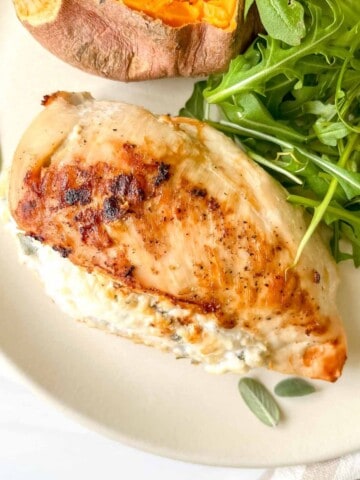 ricotta stuffed chicken breast on a cream plate next to herbs, arugula and sweet potato.