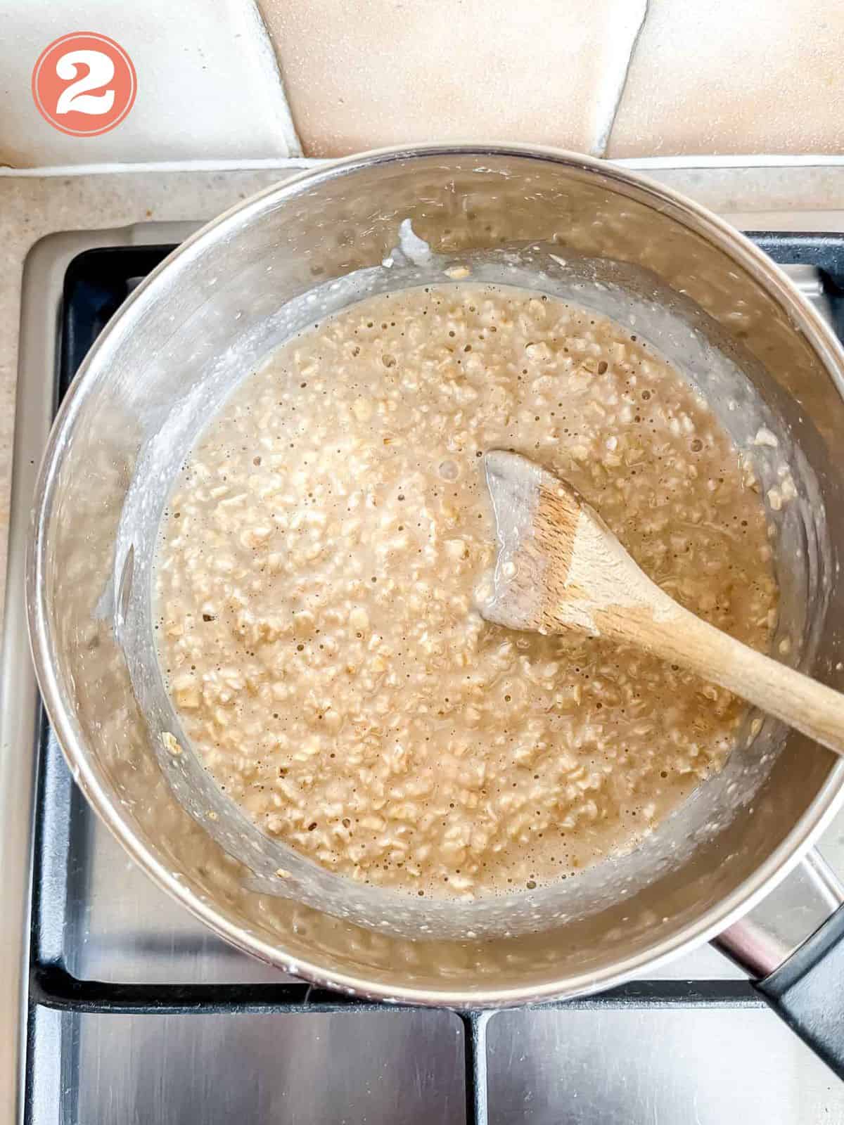 oat milk porridge cooking in a pot with a wooden spoon in it on a stove top labelled number two.