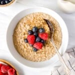 oat milk porridge in a white bowl with a spoon in it next to a bowl of raspberries.