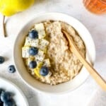 coconut milk porridge in a cream bowl with a wooden spoon next to blueberries and pears.