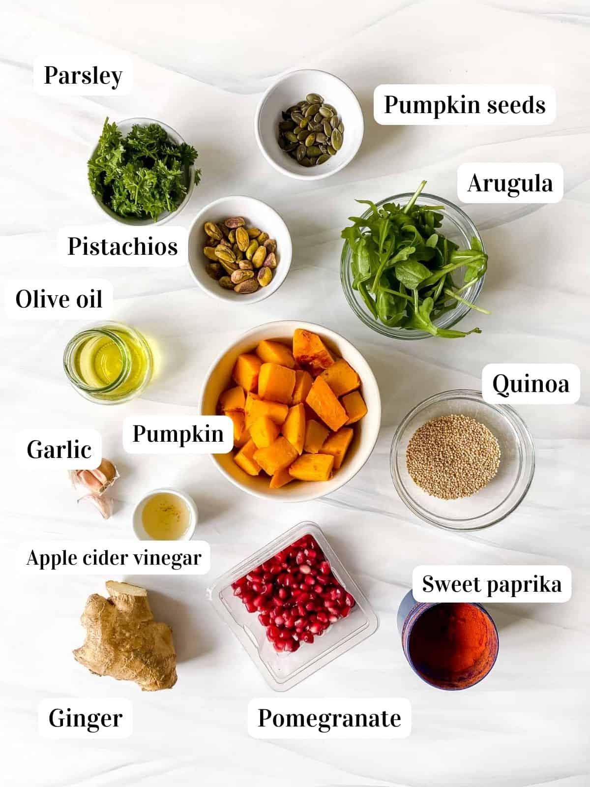 individually labelled ingredients to make pumpkin quinoa salad including olive oil, pistachios, pomegranate, ginger and arugula.
