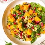 pumpkin quinoa salad on a light cream plate garnished with pomegranate seeds.