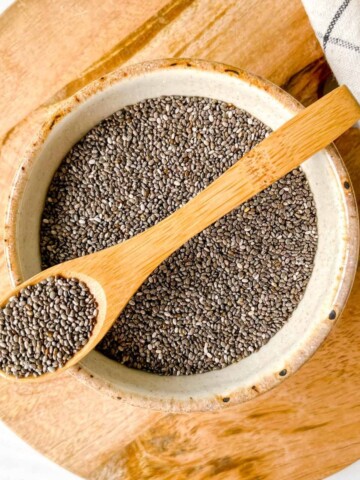 bowl of chia seeds with a wooden spoon on top on a round wooden board.
