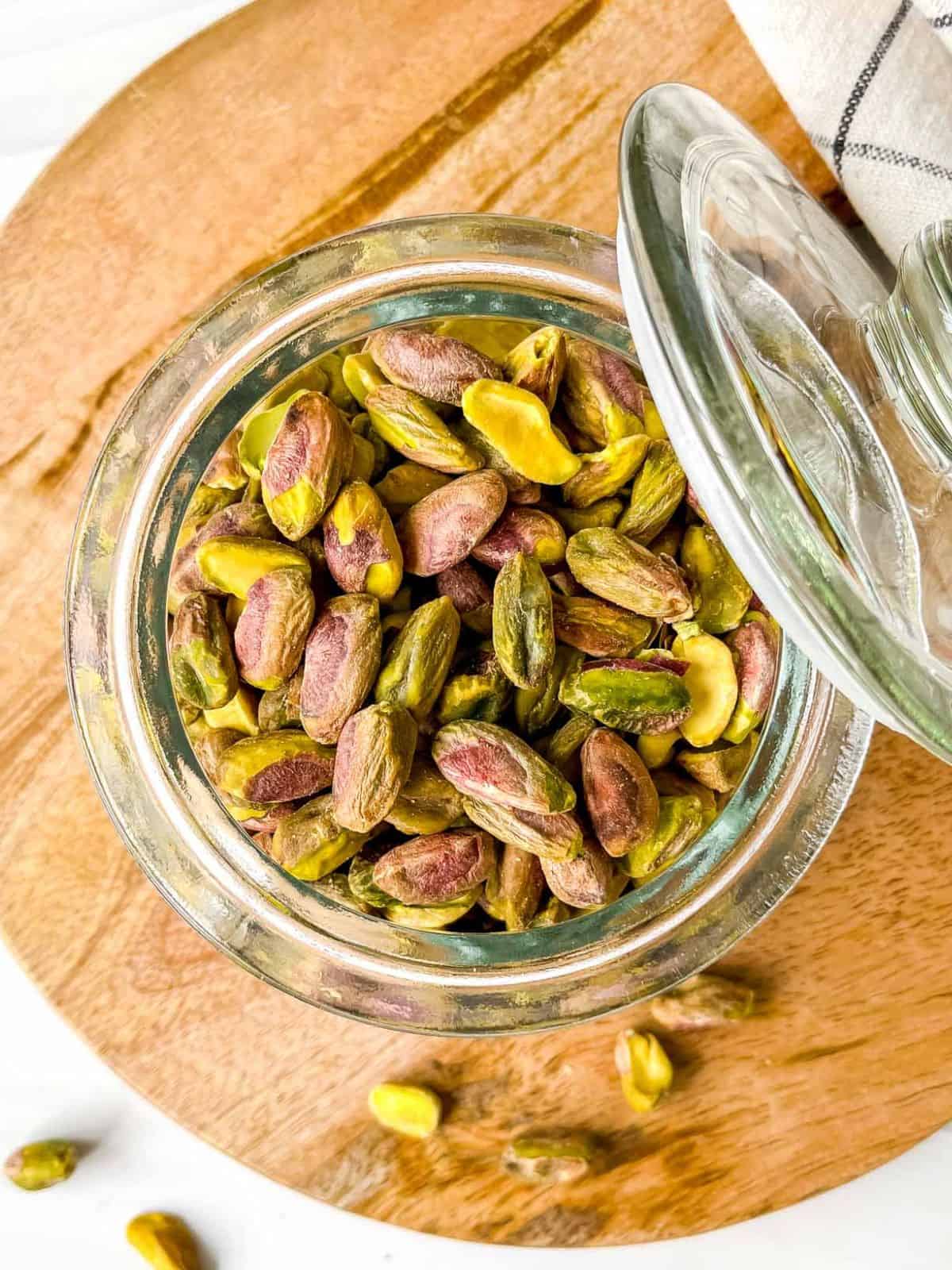 pistachios in a glass jar on a round wooden board.